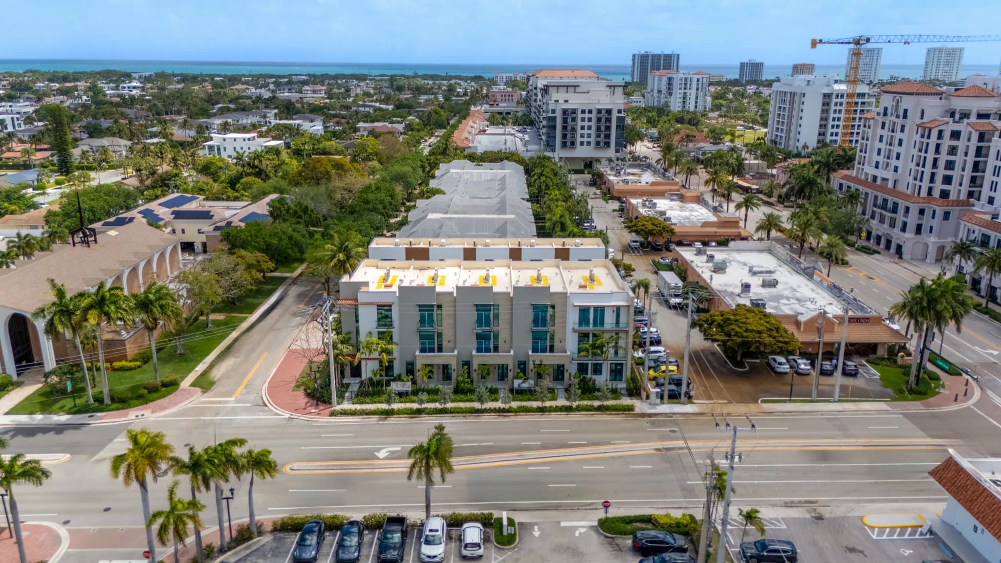 Aerial view of modern white townhome buildings near ocean with palm-lined streets and downtown towers