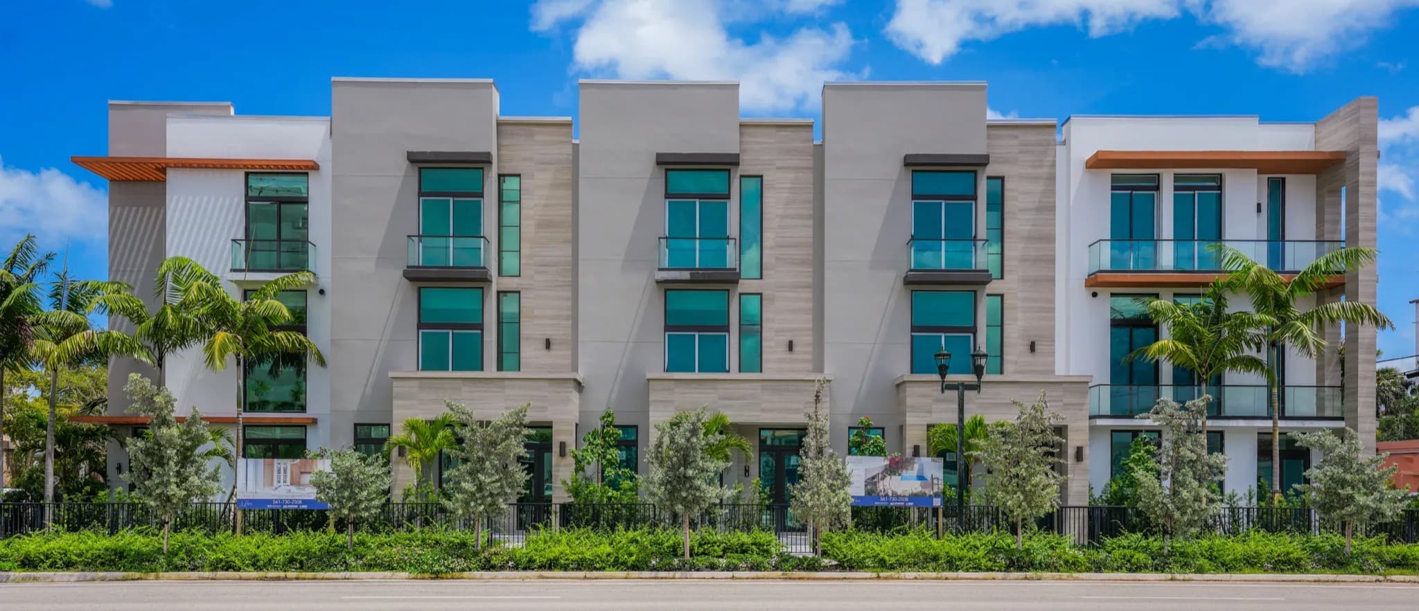 Wide street-level view of the modern white Le Rêve townhome row with palm trees and balconies under blue sky
