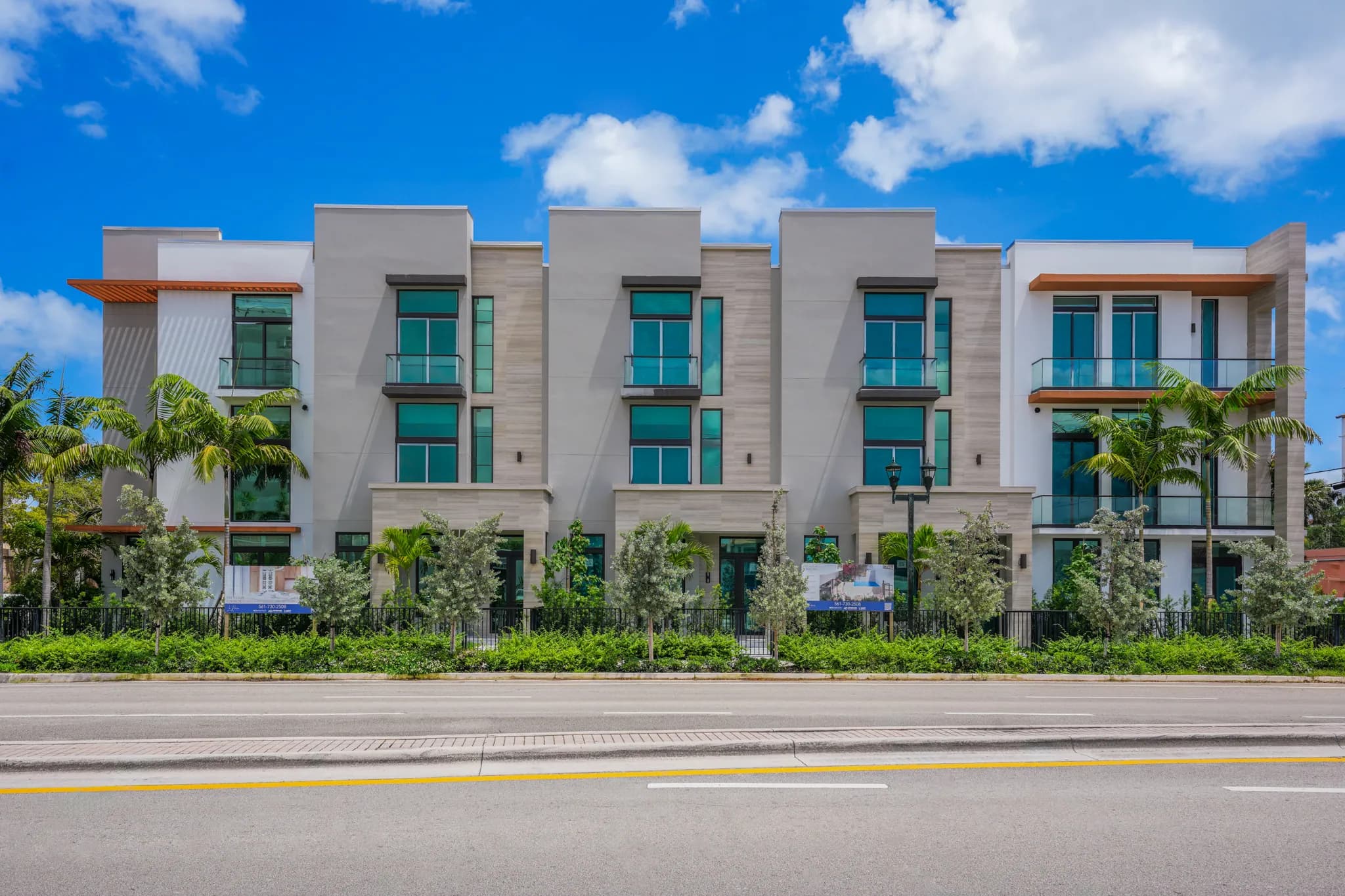 Street-facing facade of contemporary townhomes with floor-to-ceiling glass and landscaped hedges
