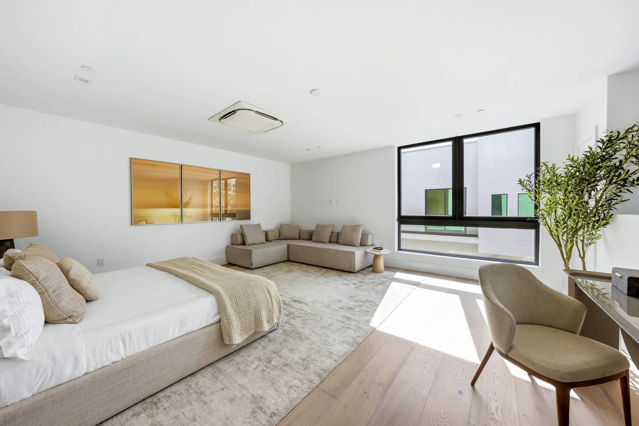 Primary bedroom with upholstered bed, sectional sofa, and wide oak flooring