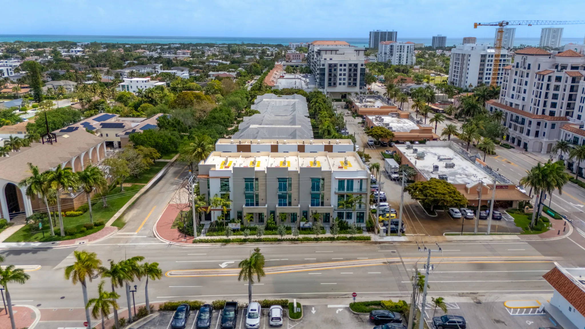 Aerial view of modern white townhome buildings near ocean with palm-lined streets and downtown towers