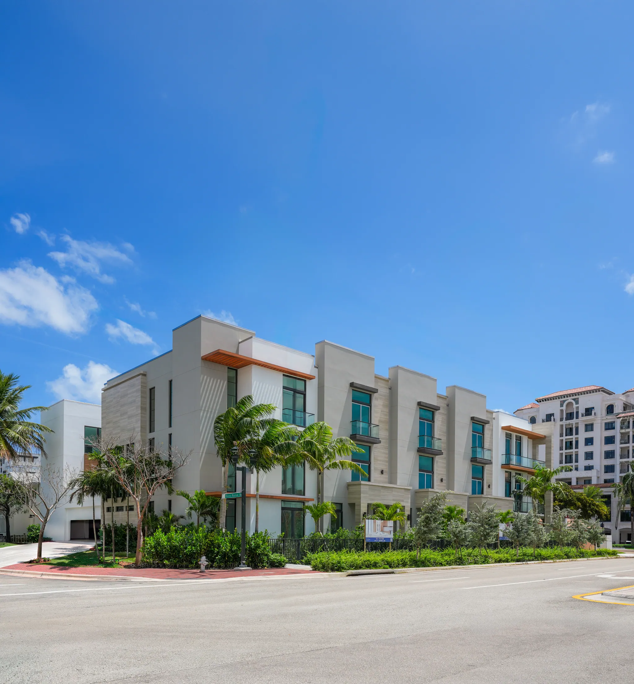 Corner view of three-story modern white townhomes with palm trees against bright blue sky