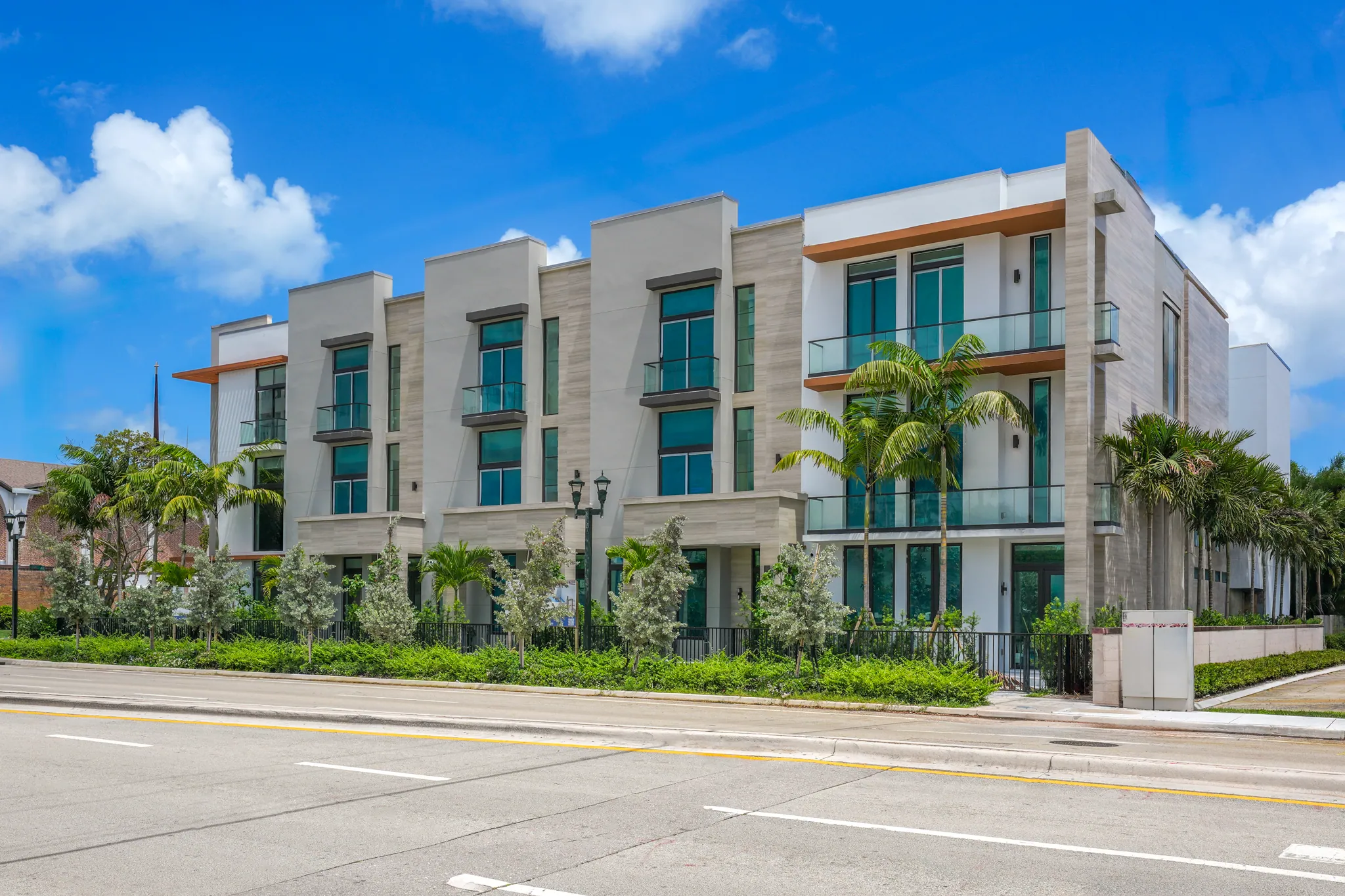 Angled facade of modern townhomes with stone accents, palm trees and balconies in daylight