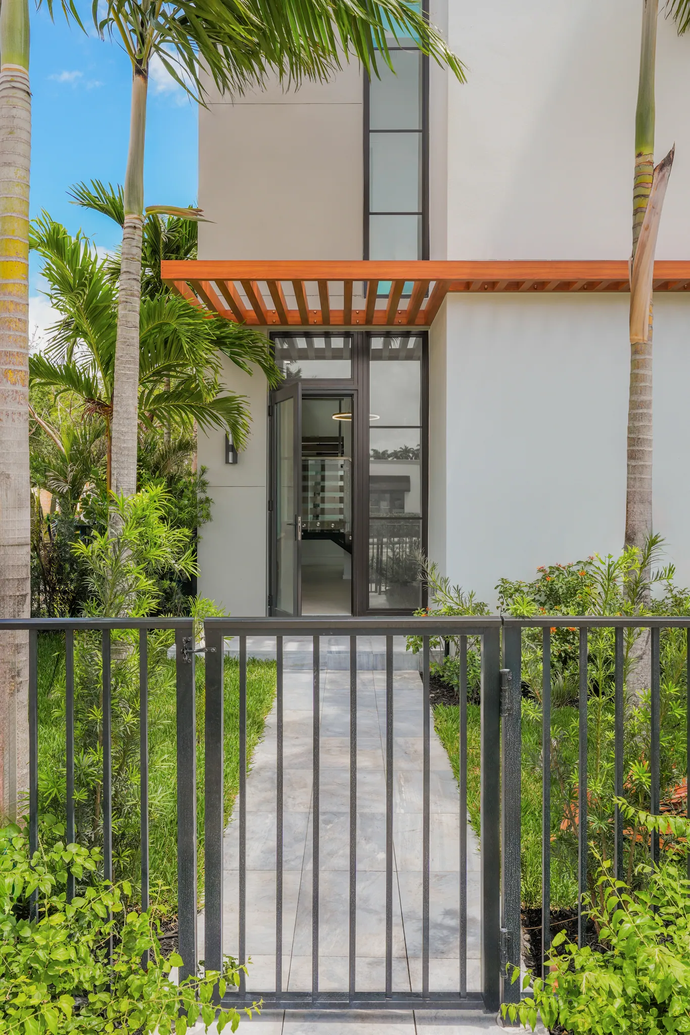 Pedestrian gate entry with stone path leading to glass front door under wood pergola canopy