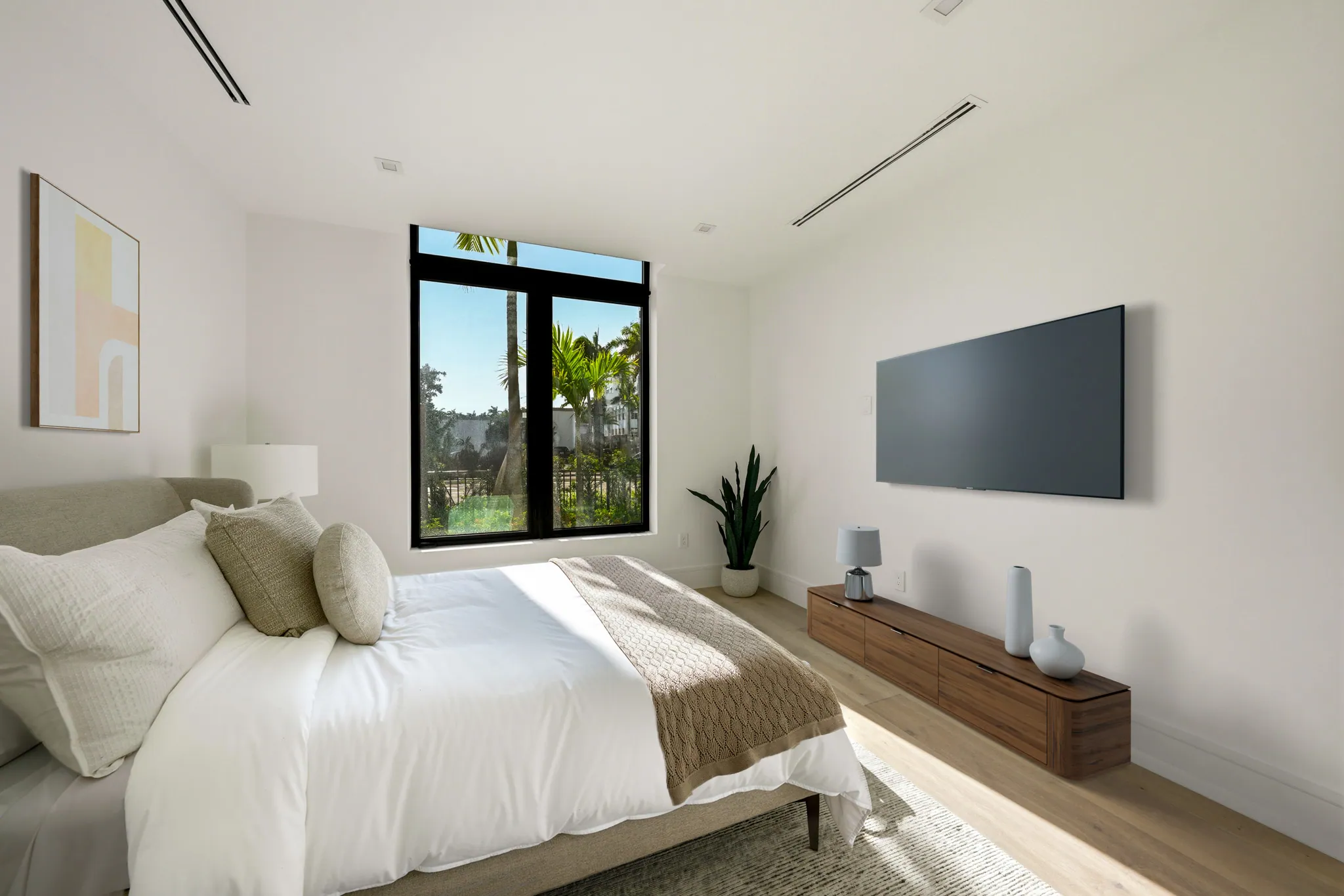 Bedroom with upholstered bed, wall-mounted television, and palm-framed window