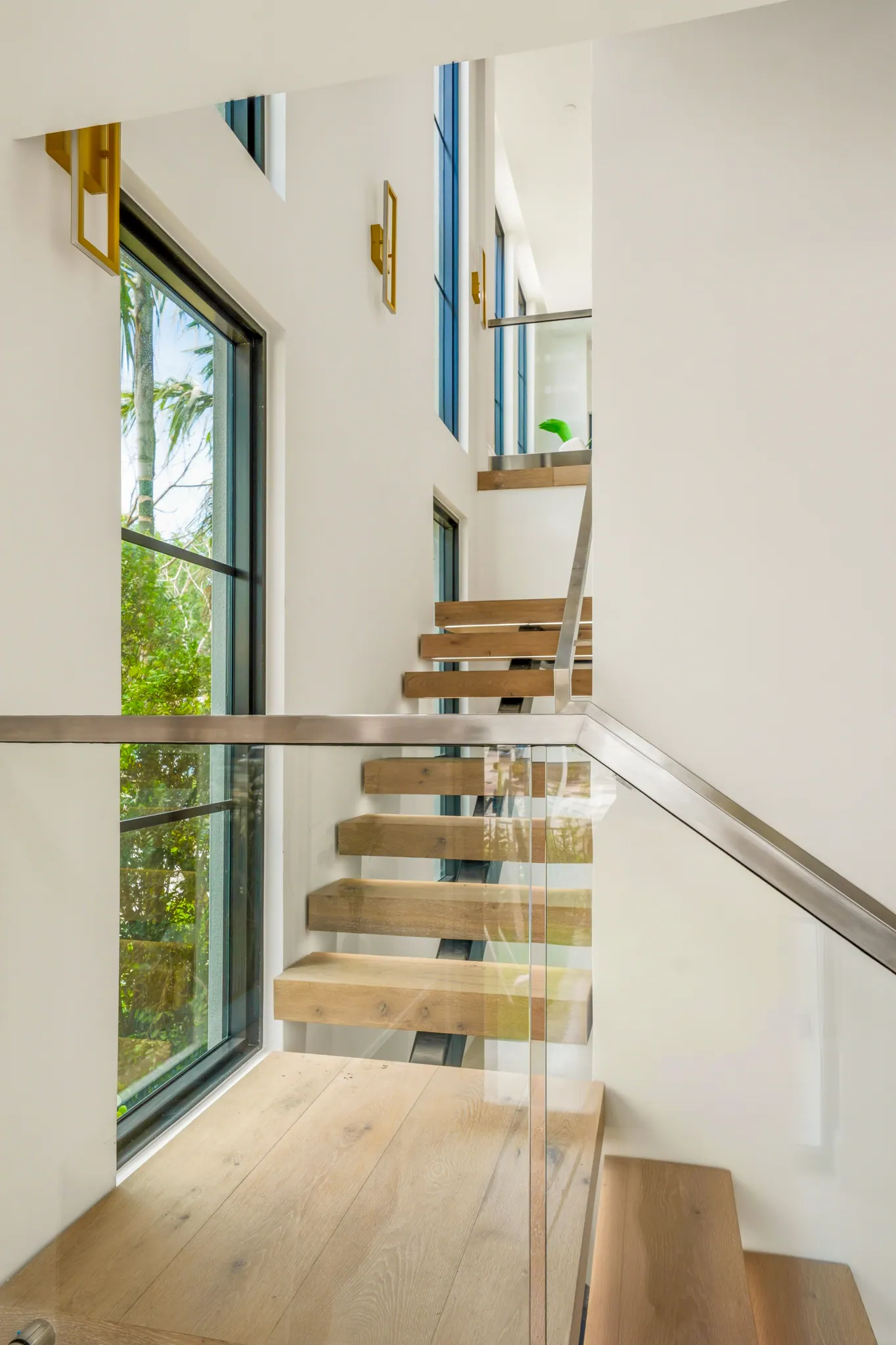 Floating oak staircase with glass railings beside floor-to-ceiling window