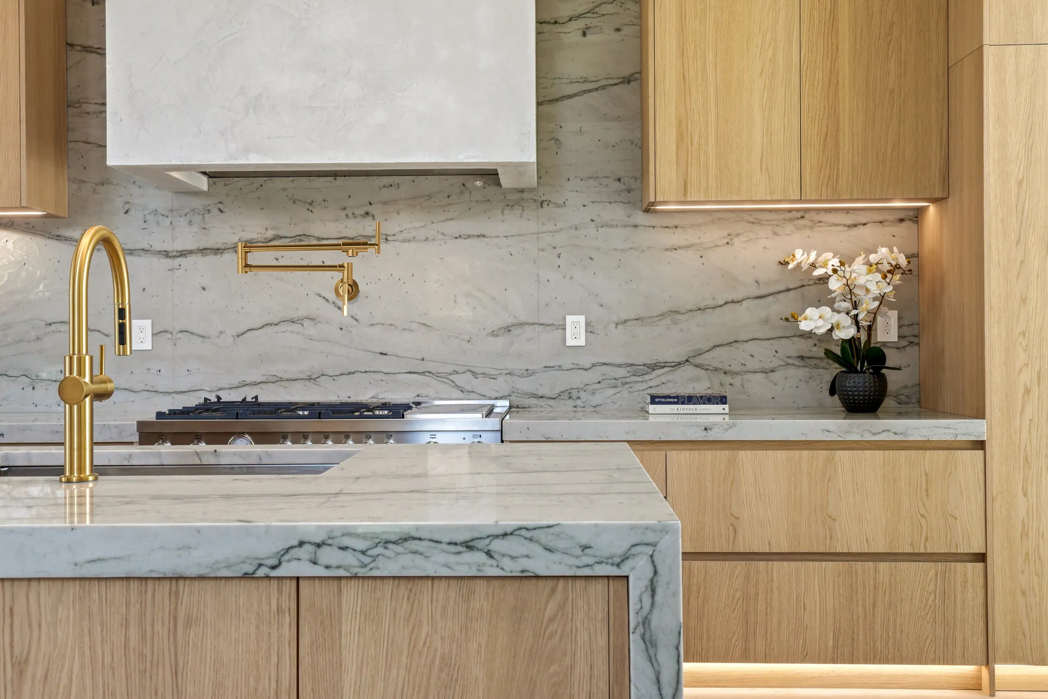 Kitchen detail with quartzite backsplash, brass pot filler, and gas cooktop