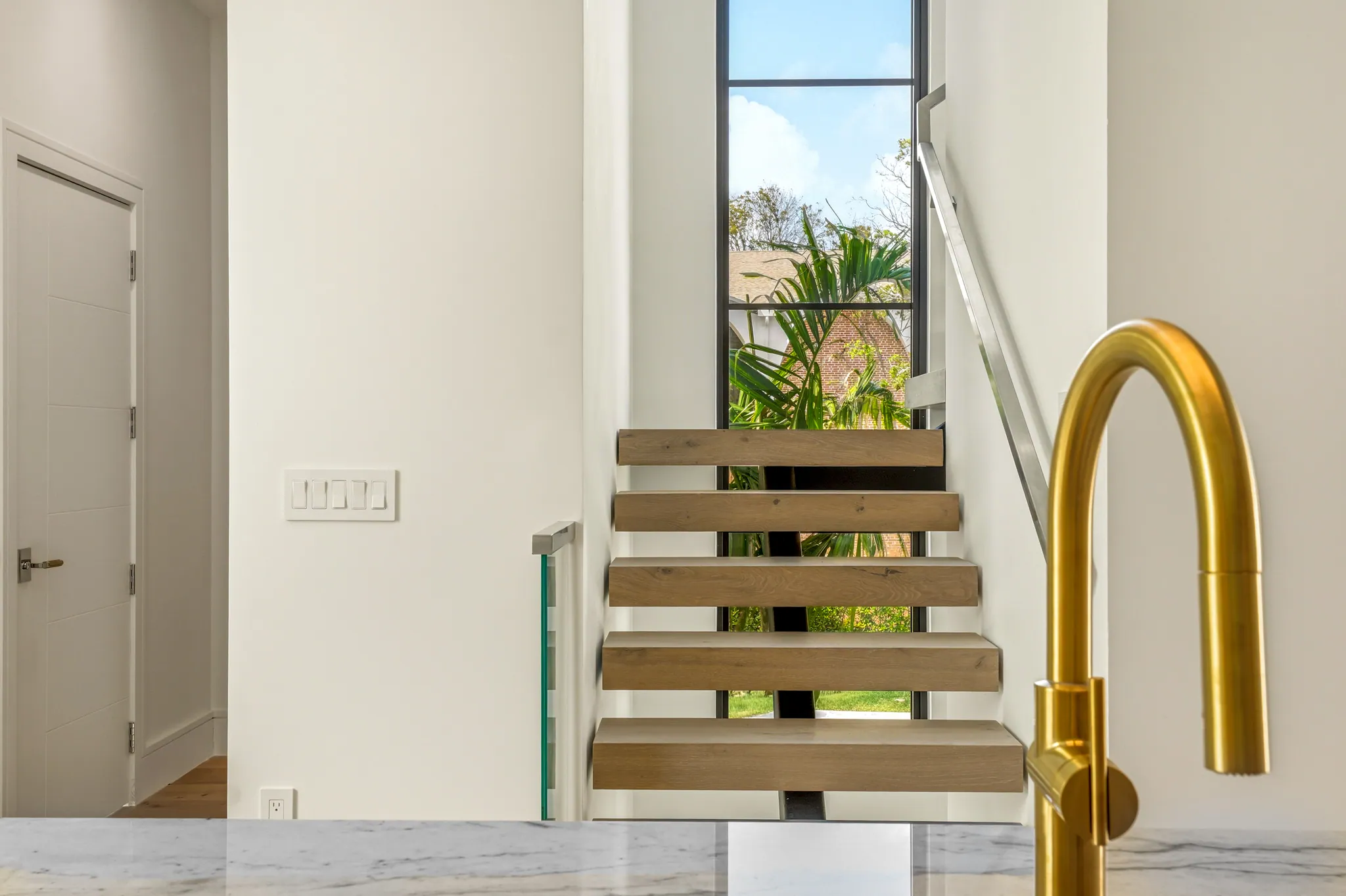 Floating white oak staircase with full-height window beside marble waterfall island