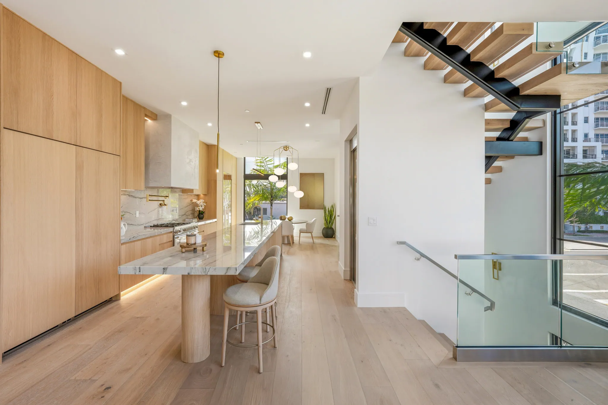 Kitchen island and breakfast bar adjacent to floating staircase and glass railing