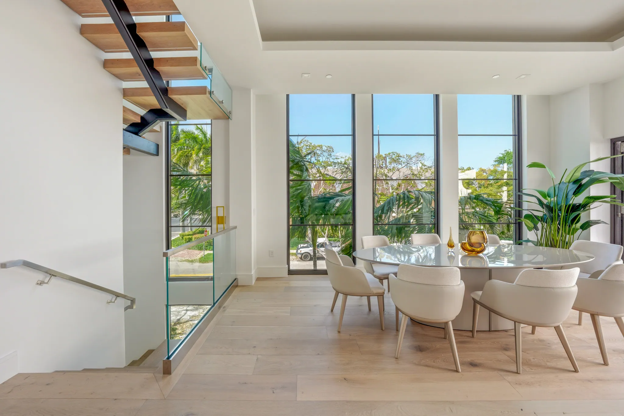 Dining area beside floating stair with glass railing and tall casement windows