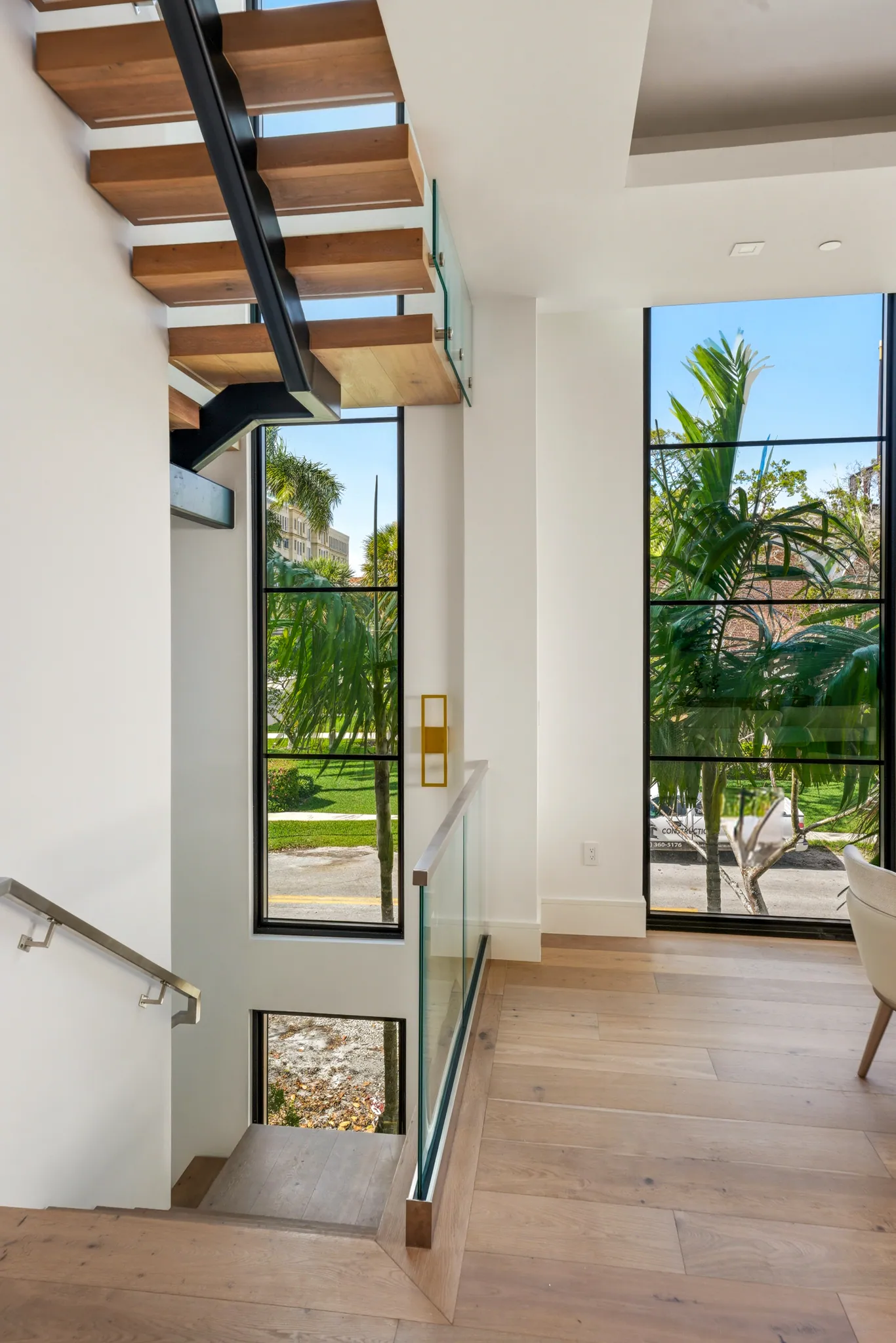Stair landing with floating treads, glass railing, and tall steel-framed windows