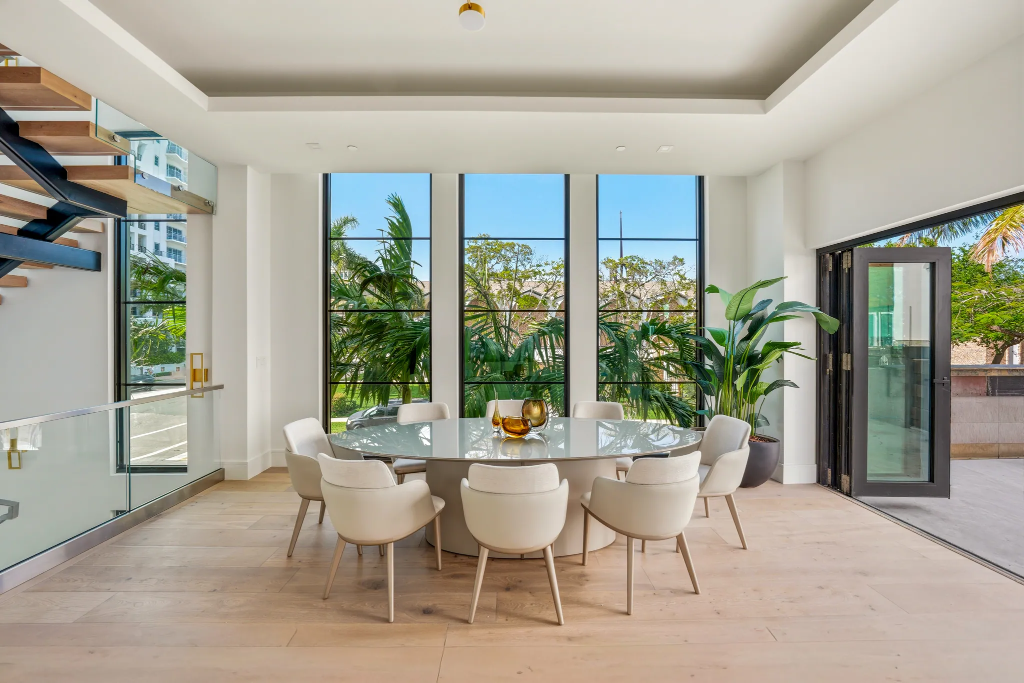Dining area with oval table, eight chairs, and floor-to-ceiling steel windows