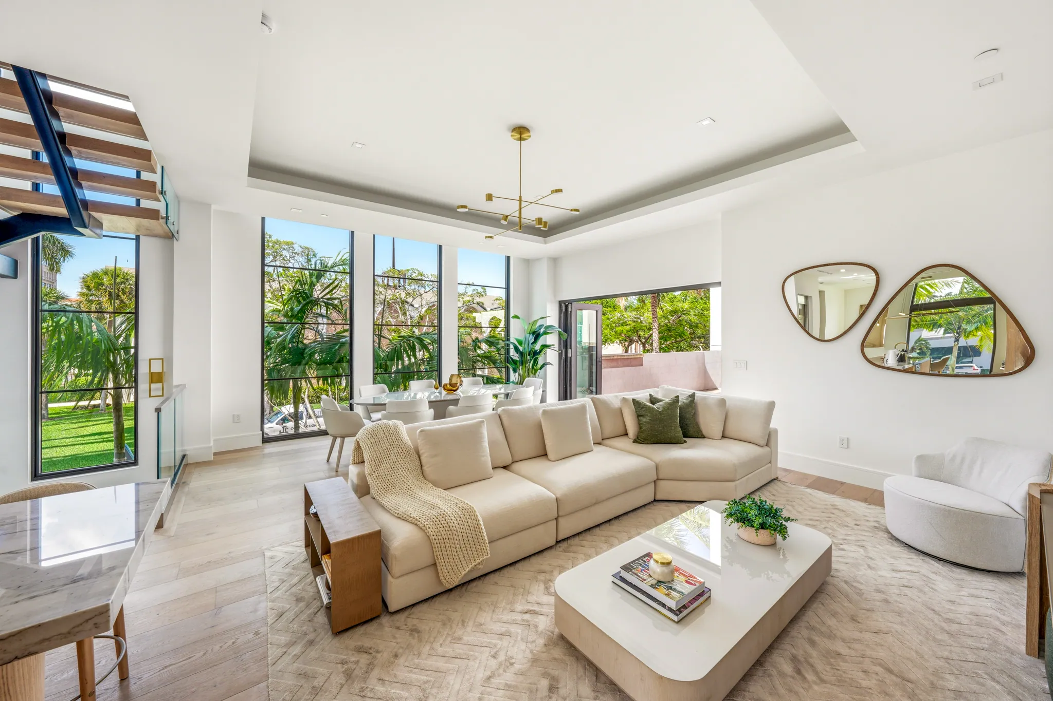 Open great room with sectional sofa, sculptural mirrors, and tall glass windows