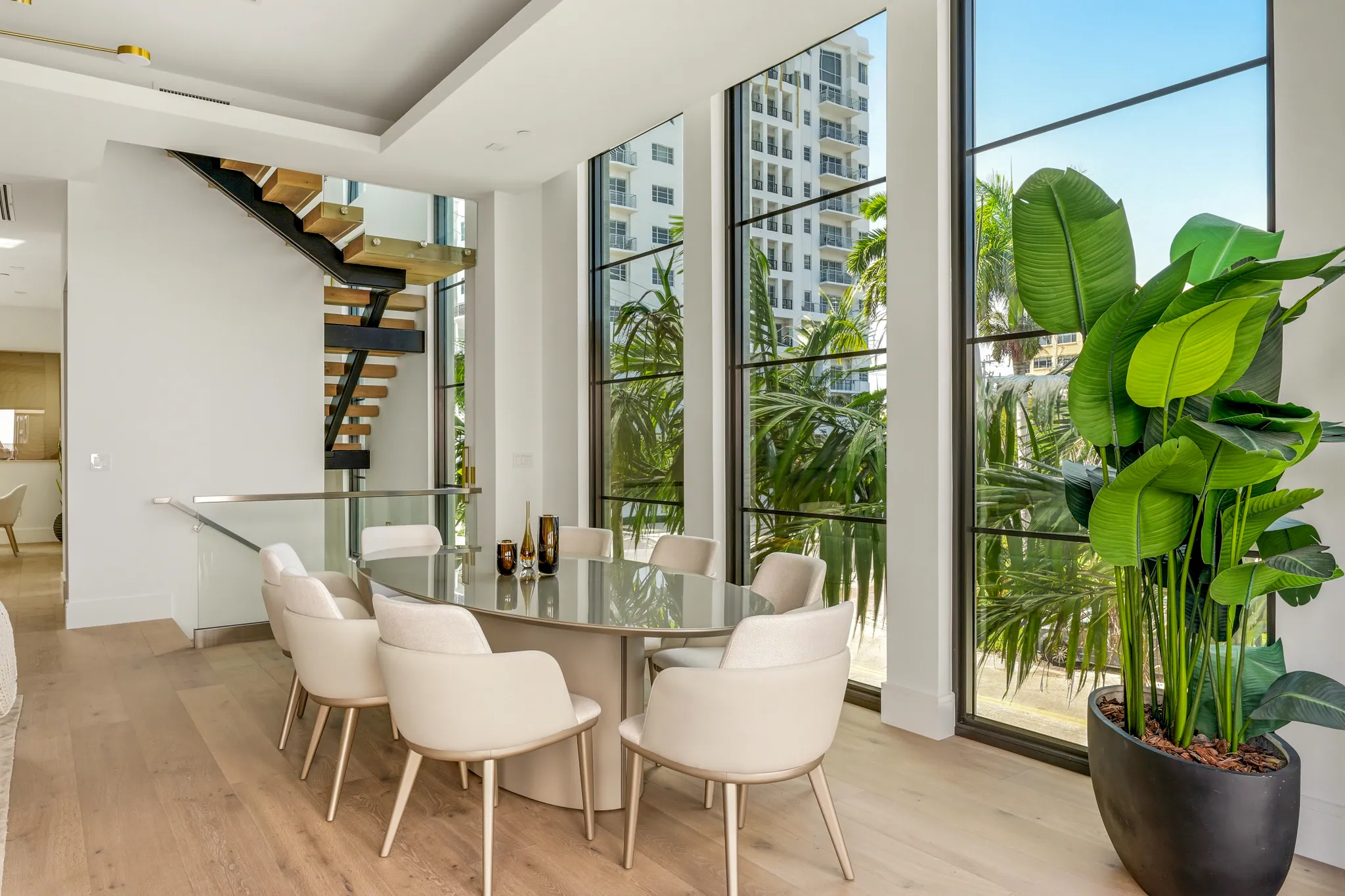 Dining nook with oval table, floating staircase, and tall steel-framed windows