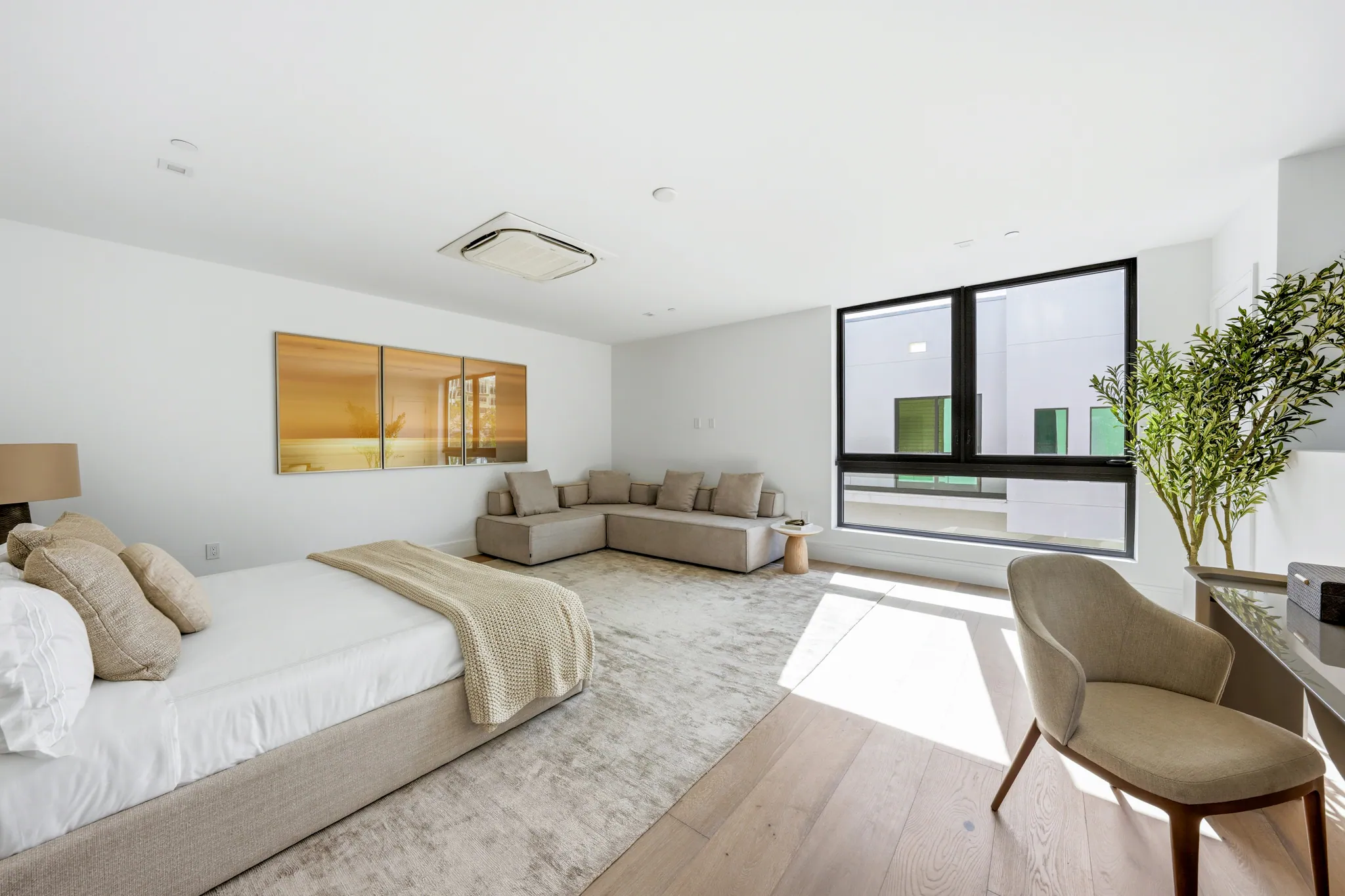 Primary bedroom with upholstered bed, sectional sofa, and wide oak flooring