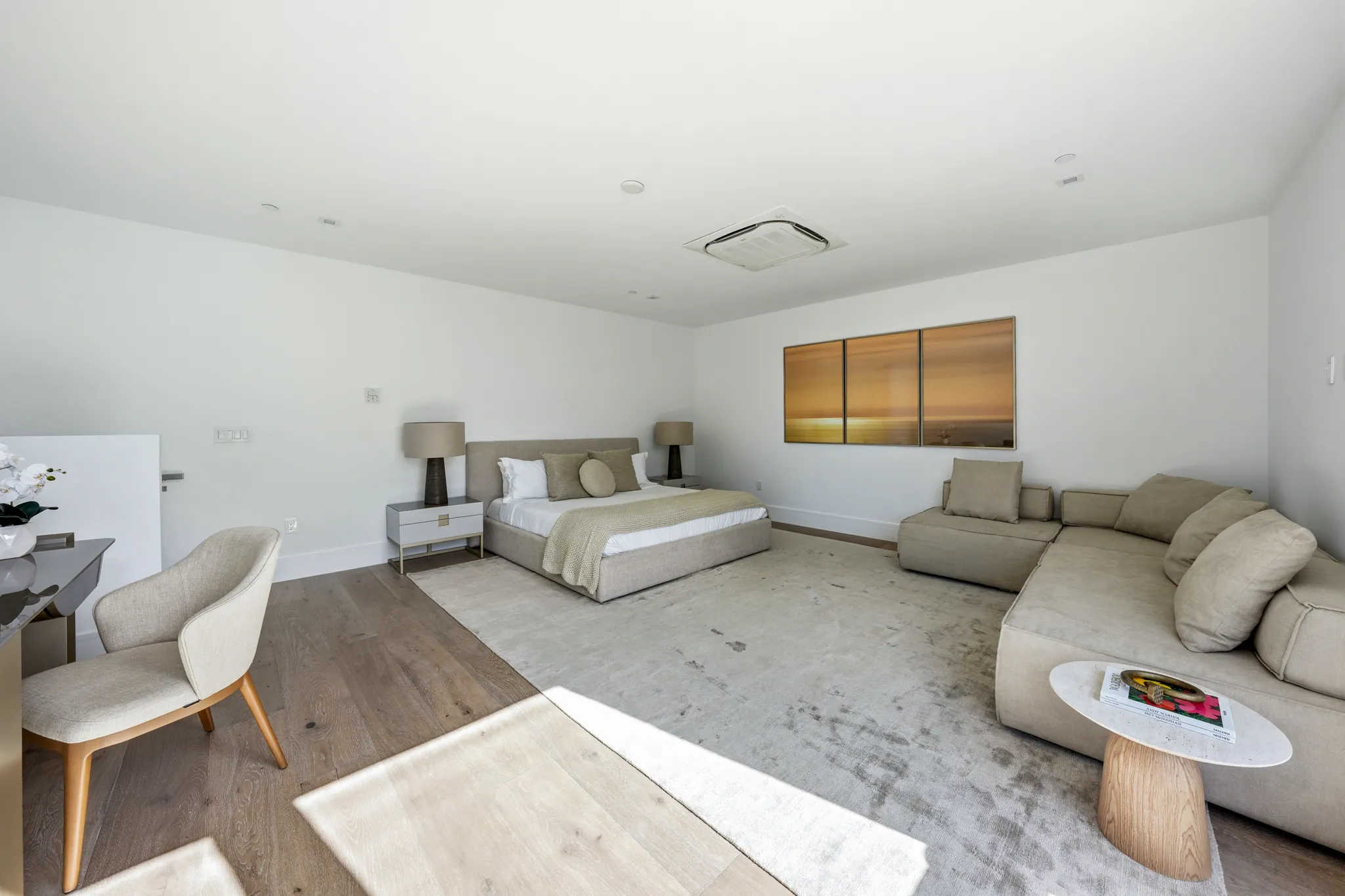 Spacious primary suite with bed, lounge sectional, and triptych artwork