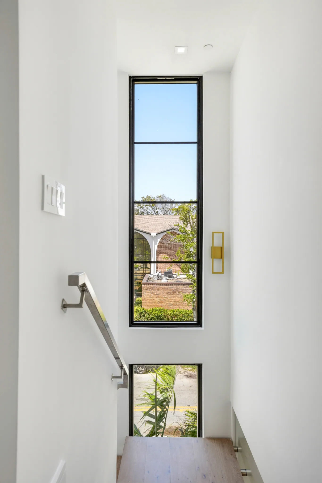 Stair landing with steel-framed window and brushed metal handrail above white oak floors