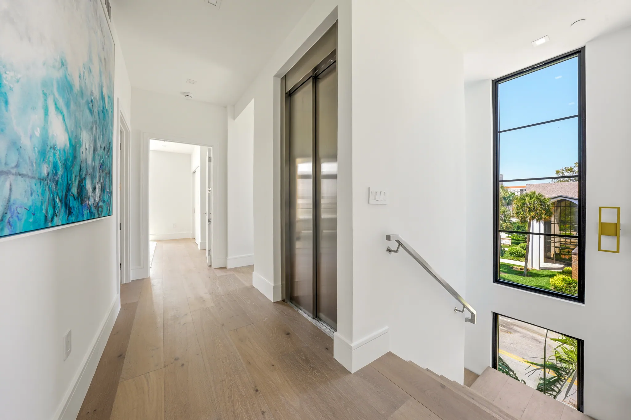 Upper hallway with elevator, white oak floors, and steel-framed window to garden