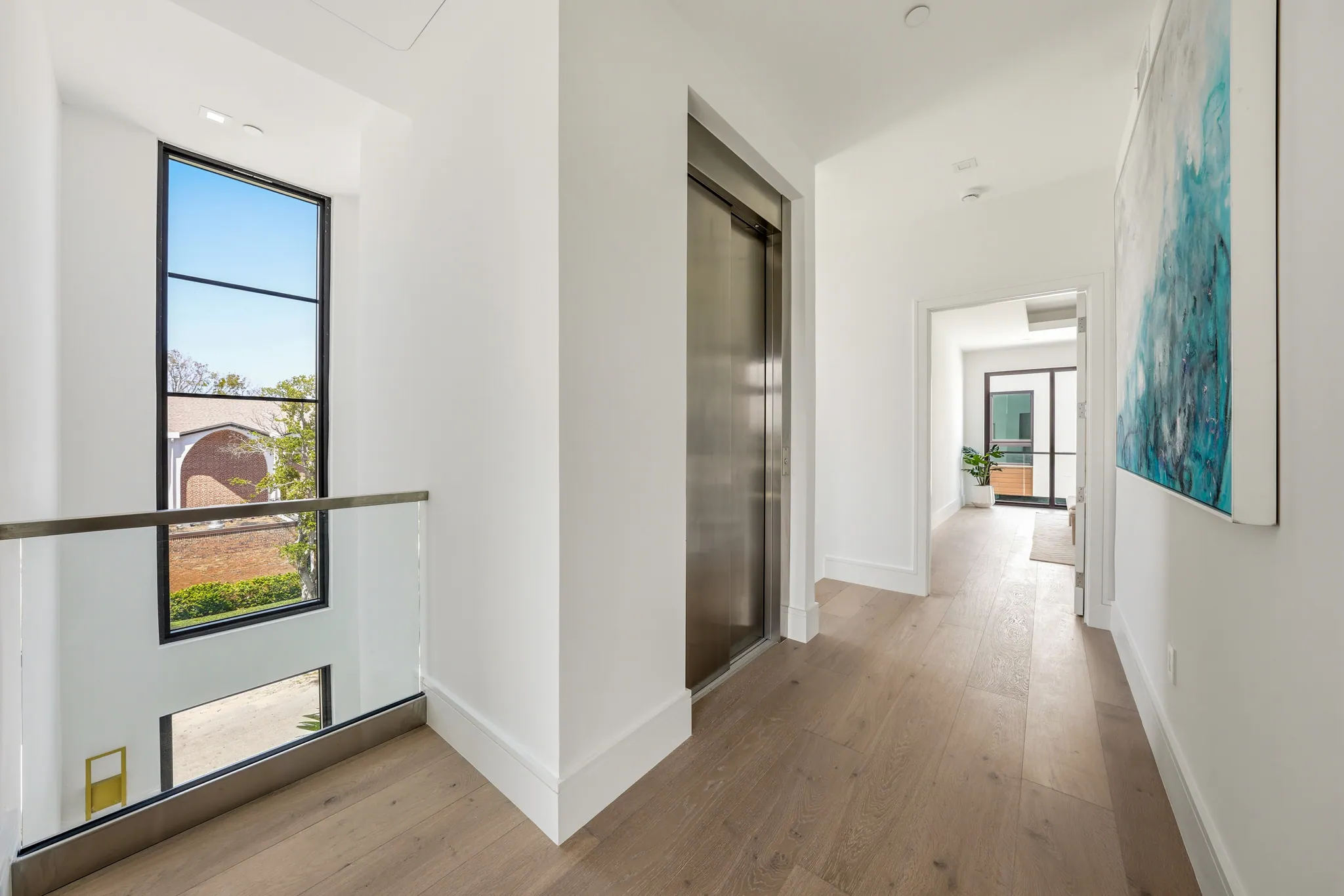 Second-floor corridor with elevator, abstract artwork, and tall steel-framed stairwell window