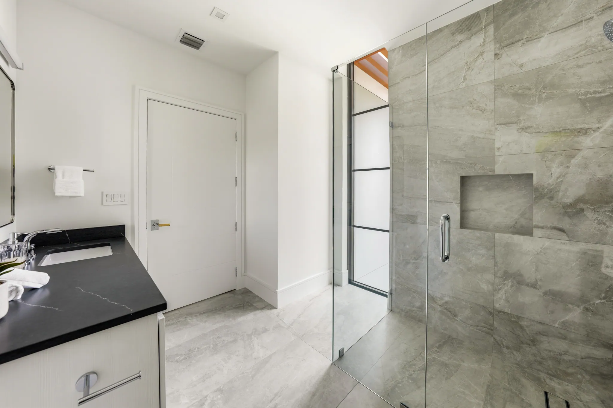 Secondary bath with frameless glass shower, gray porcelain tile, and black stone vanity