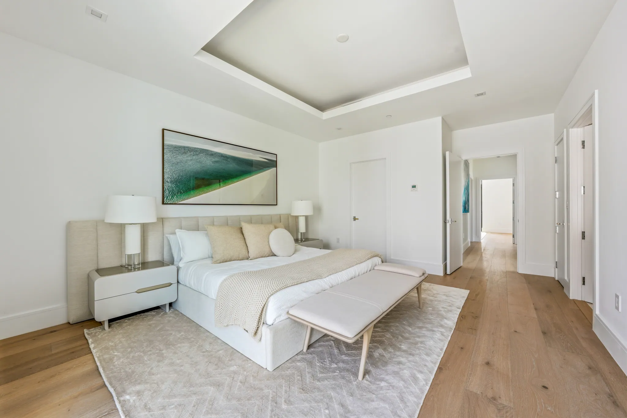Primary bedroom with tray ceiling, king bed, bench seating, and hallway sightline