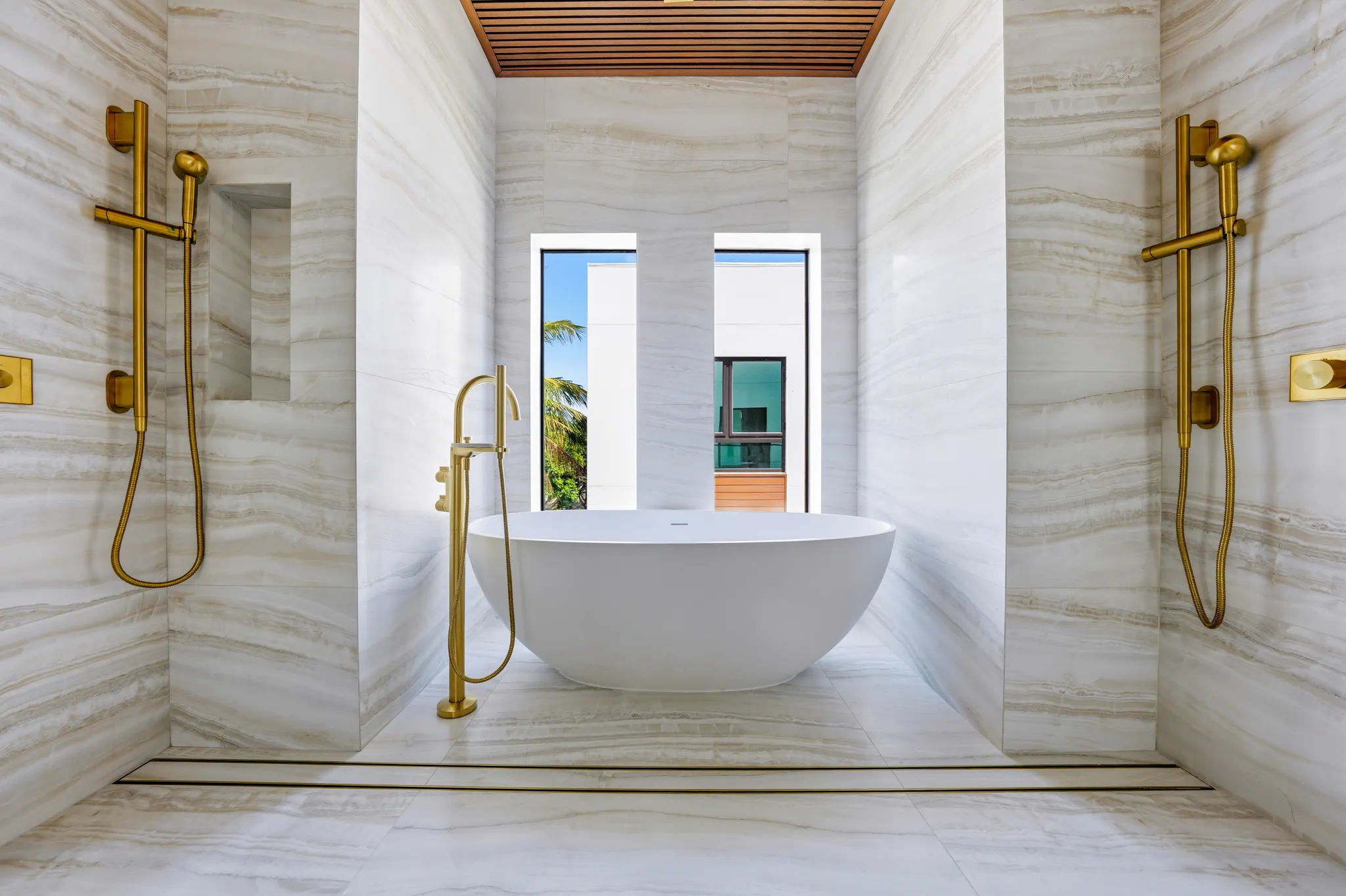 Sculpted soaking tub framed by twin brass shower fixtures and stone
