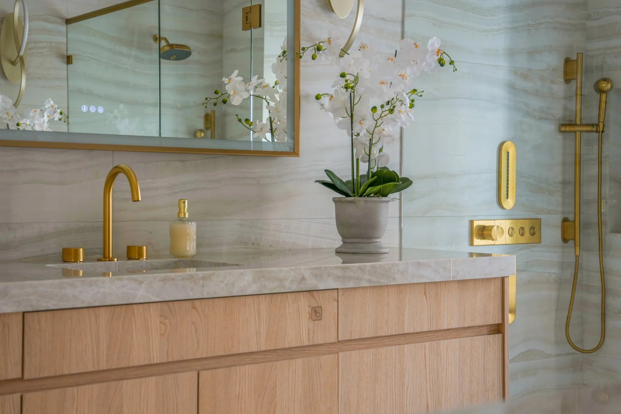 Primary vanity detail with orchid styling beside glass shower enclosure