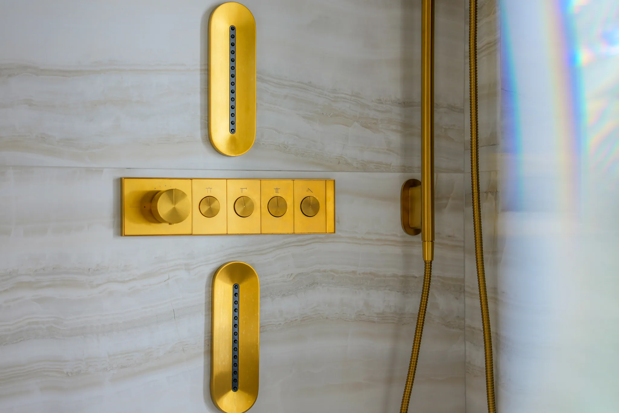 Brushed brass shower controls and body jets on travertine stone wall