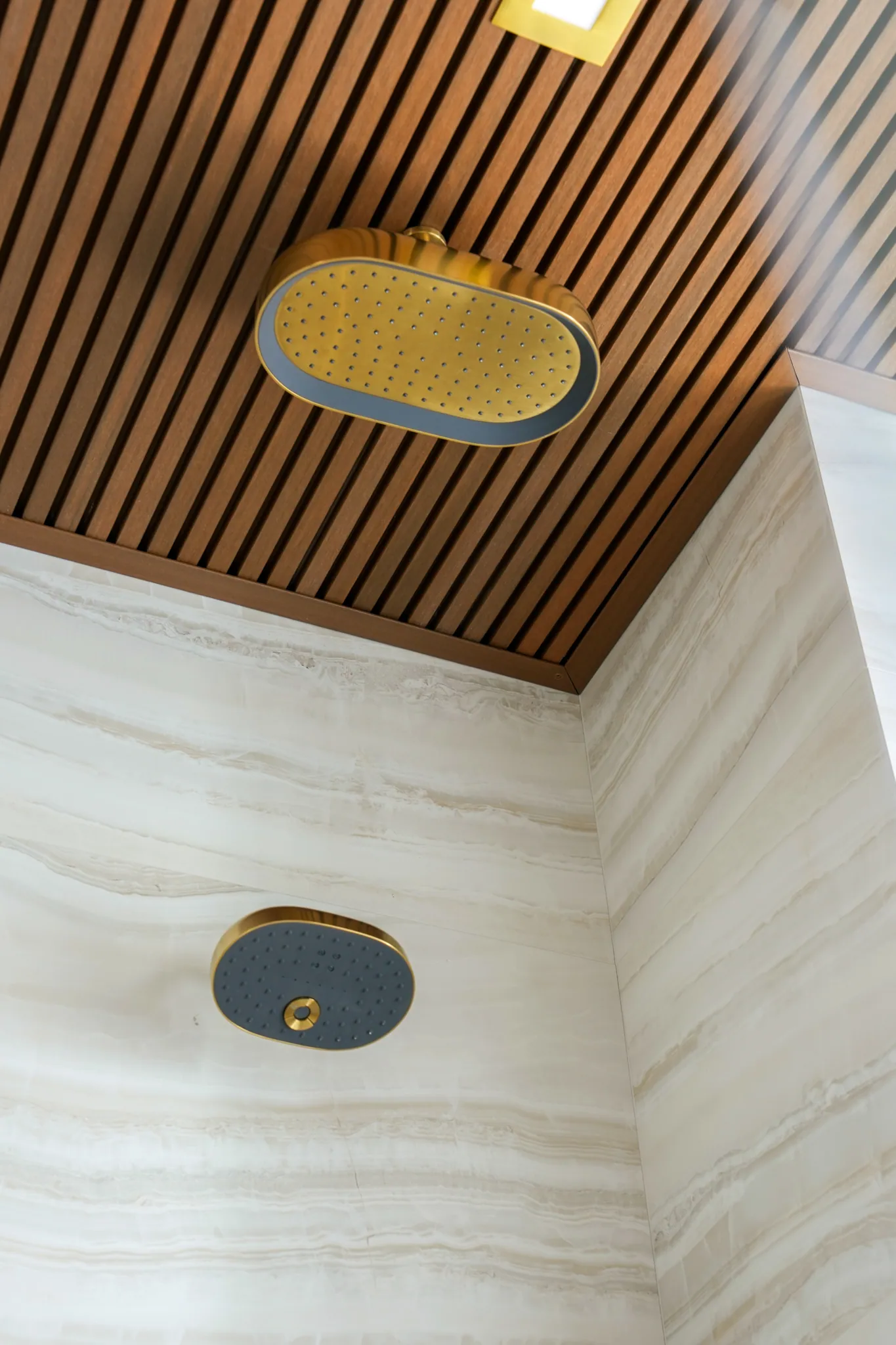 Slatted wood ceiling with brass rain shower head and wall fixture