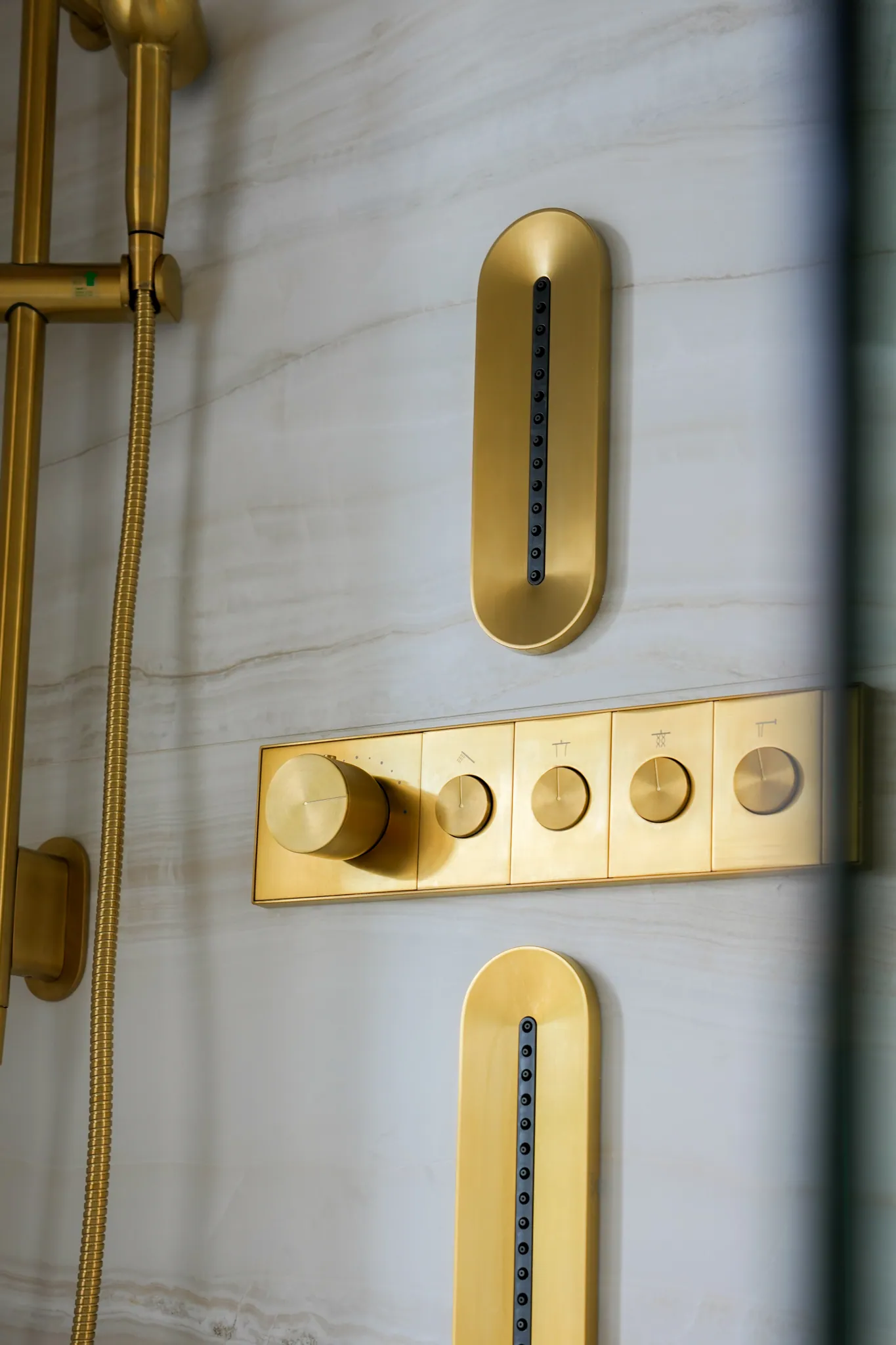 Detail of brushed brass shower valves and body sprays on marble