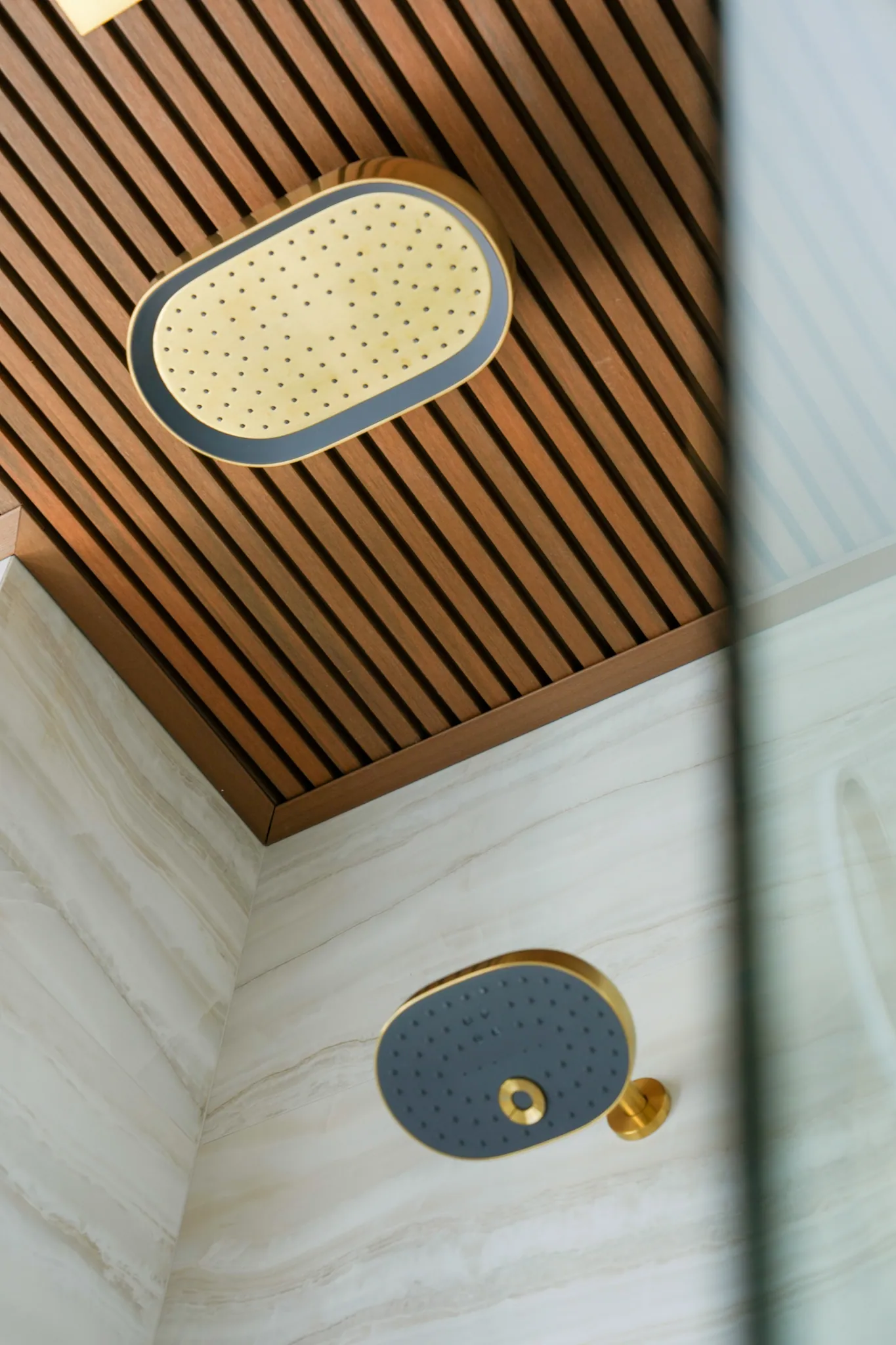 Brass rainfall shower set into wood-slat ceiling above stone walls