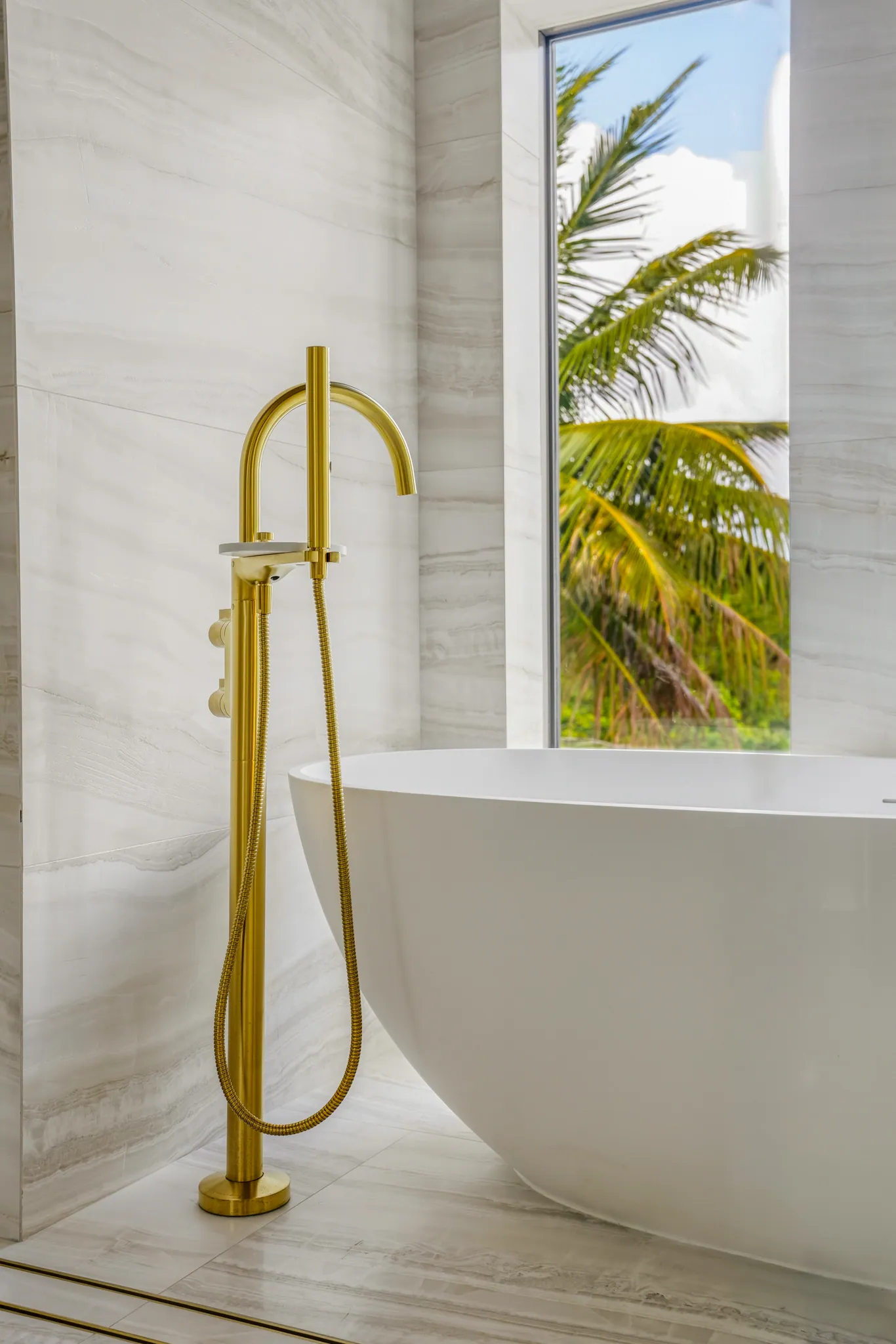 Freestanding soaking tub with brass filler framed by tropical window