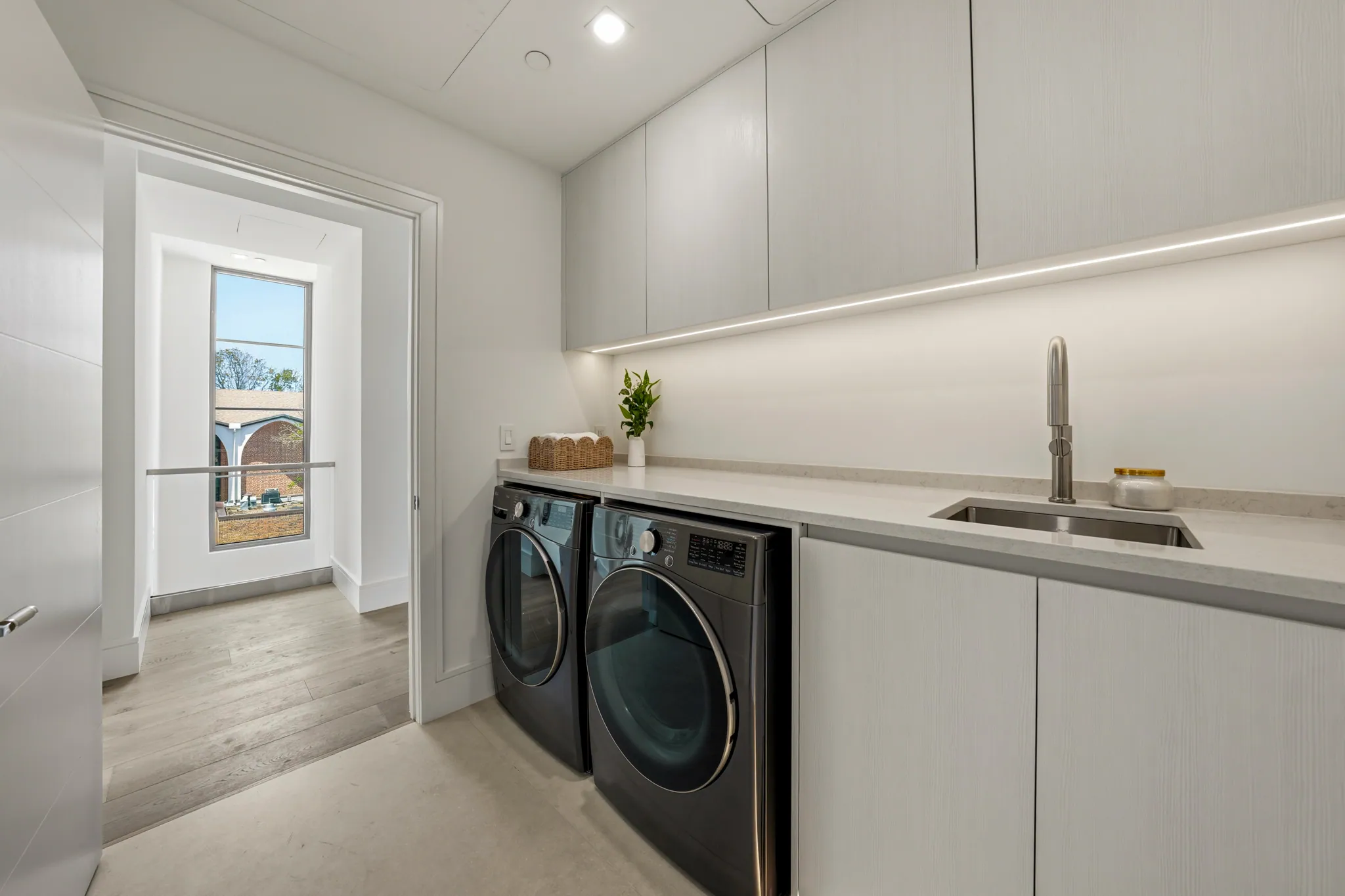 Laundry room with washer dryer pair, sink, and hallway view beyond